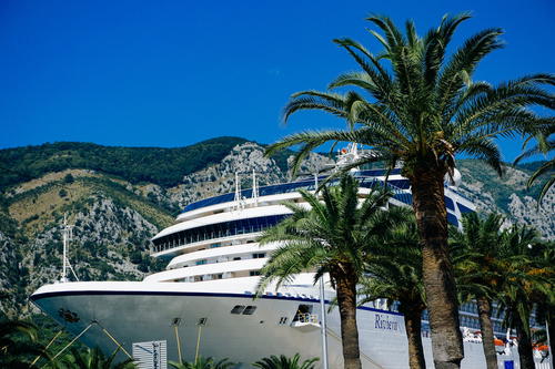 A cruise ship with palm trees in the front and mountains in the background