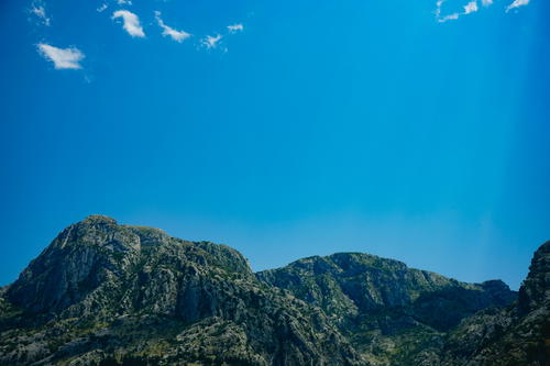A plane flying over a mountain range under a blue sky in Budva
