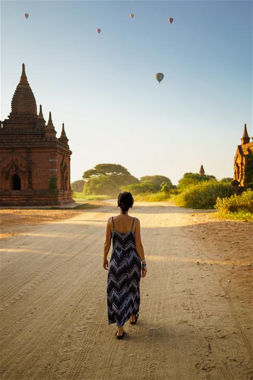 Woman walking on dirt road between Buddhist pagodas Bagan Myanmar Burma
