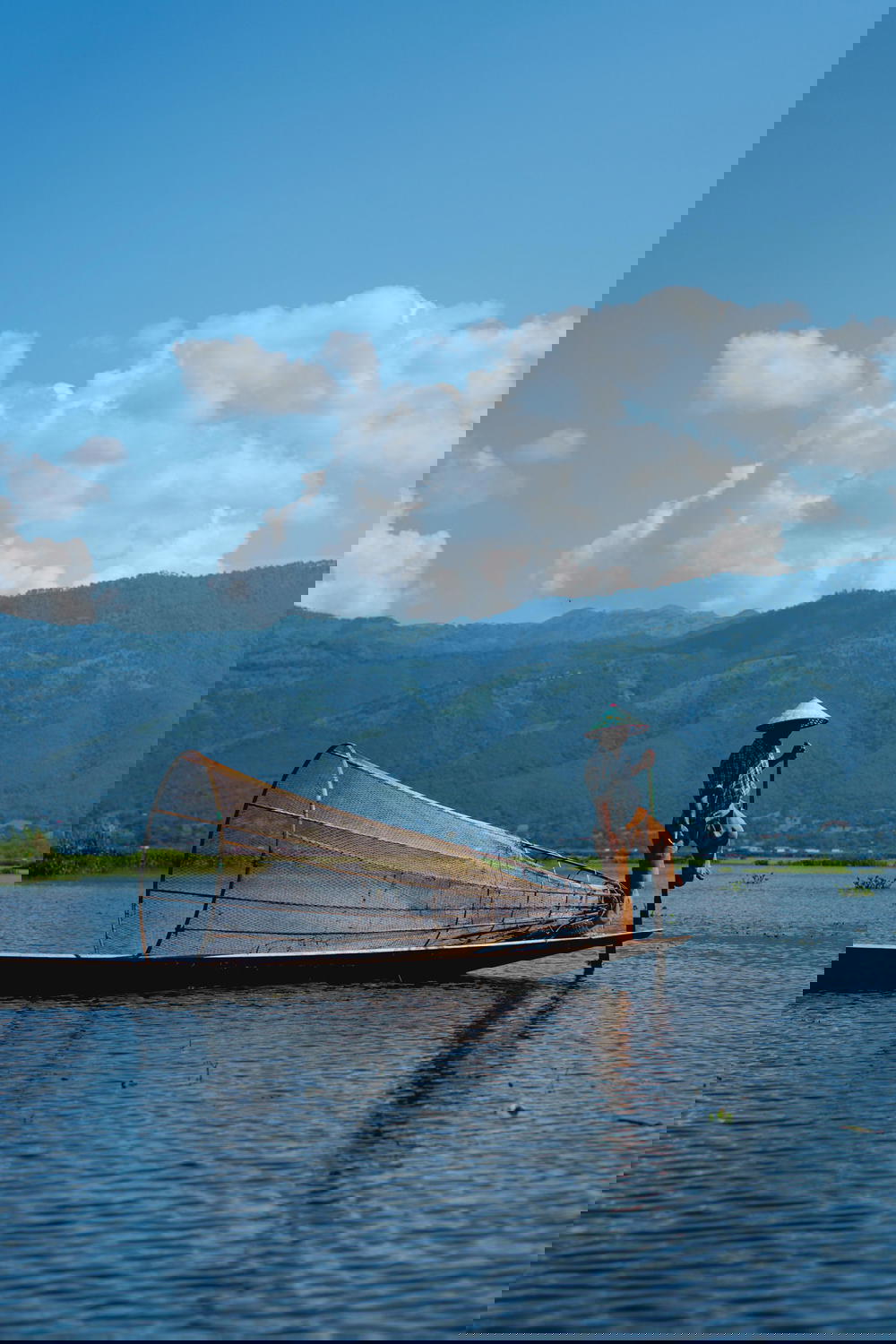 Burmese dancing fishermen standing at one end of his boat on a clear sunny day at Inle Lake Myanmar