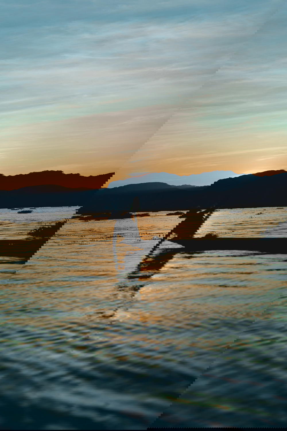 Burmese fisherman padding in his boat at sunset with mountains in the scenery at Inle Lake Myanmar