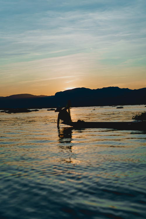 A person is sitting on a boat in Myanmar at sunset.