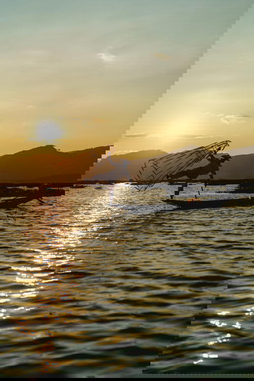 A man is fishing in a boat at sunset in Myanmar.