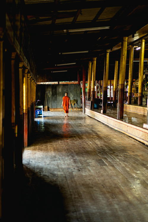 A man from Myanmar (Burma) in an orange robe walking down a hallway.