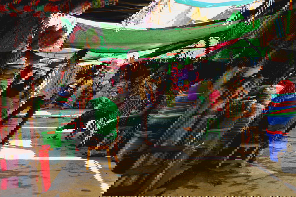 Man standing among market vendors under green tarps at the village market of Nyaungshwe Myanmar