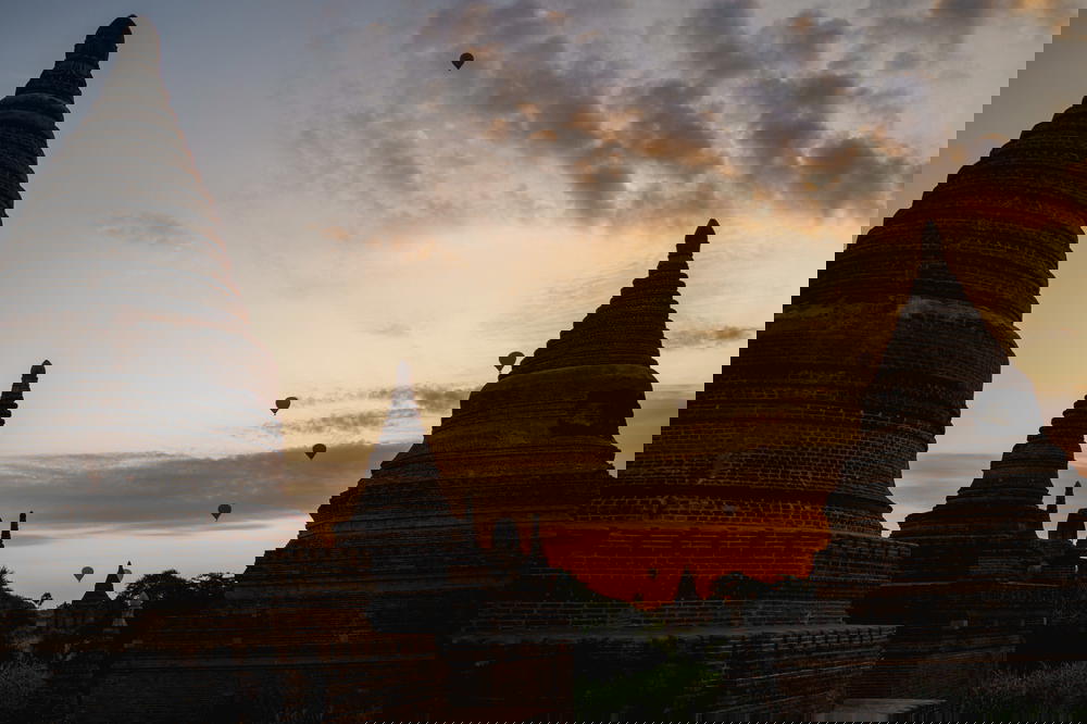 Hot air balloons going up at sunrise against a backdrop of Buddhist temple and pagoda silhouettes in Bagan Myanmar