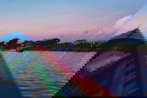 A boat is traveling down a river in Myanmar at sunset.