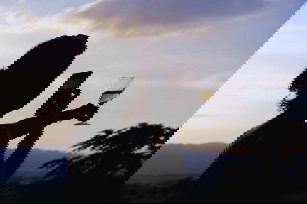 Girl taking a photo of a wine glass against a sunset backdrop with a cell phone camera in Myanmar