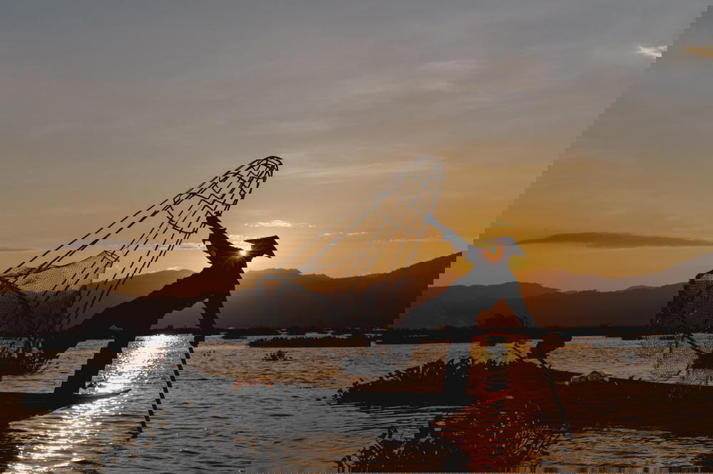 Magic golden hour at Inle Lake Myanmar as a dancing fisherman is balancing on one foot in his boat