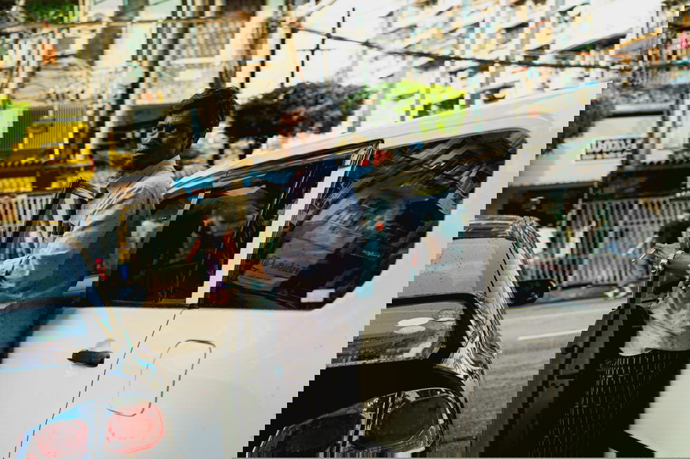 Local Burmese man holding a car door open with cigarette in hand at rush hour in Yangon Myanmar