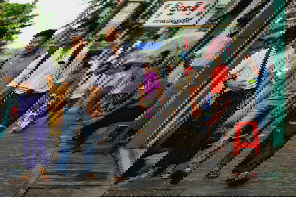 Young men in traditional and modern dress walk down a neighborhood street in Yangon Myanmar