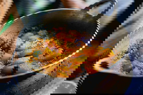 Potato pieces simmering in a brown Burmese curry in a silver pot over a wooden table
