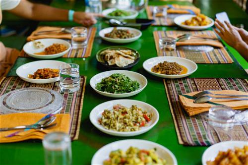 Green wooden table with place settings and white plates of Burmese salads
