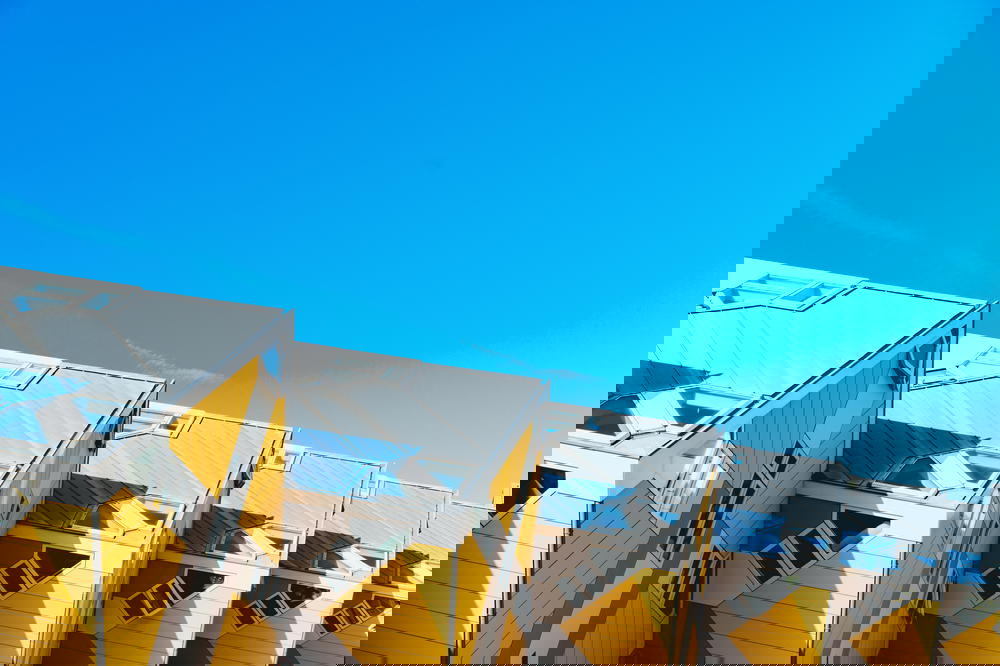 A row of yellow and white buildings showcasing Rotterdam's architecture against the backdrop of a blue sky in The Netherlands.