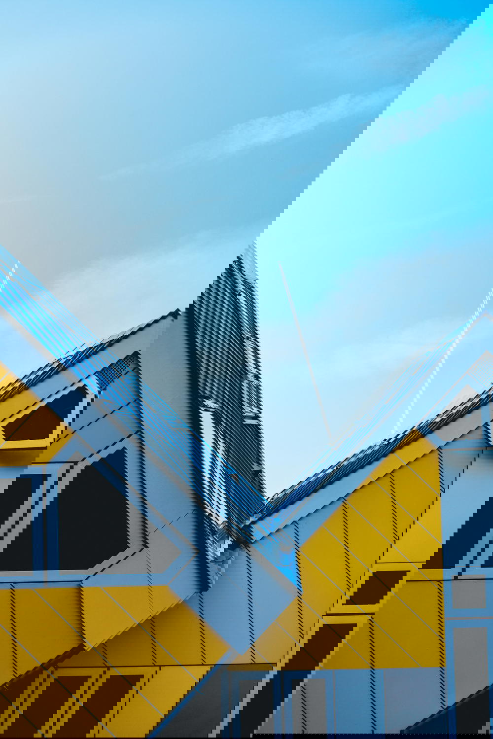 An architectural marvel in Rotterdam, The Netherlands showcasing a yellow and white house against a stunning blue sky.