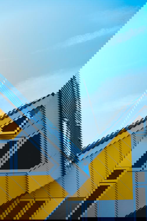 An architectural marvel in Rotterdam, The Netherlands showcasing a yellow and white house against a stunning blue sky.