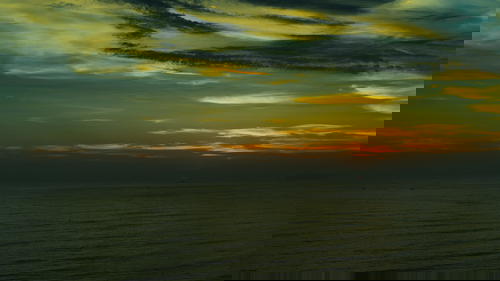 A person is flying a kite over the ocean in Peru at sunset.
