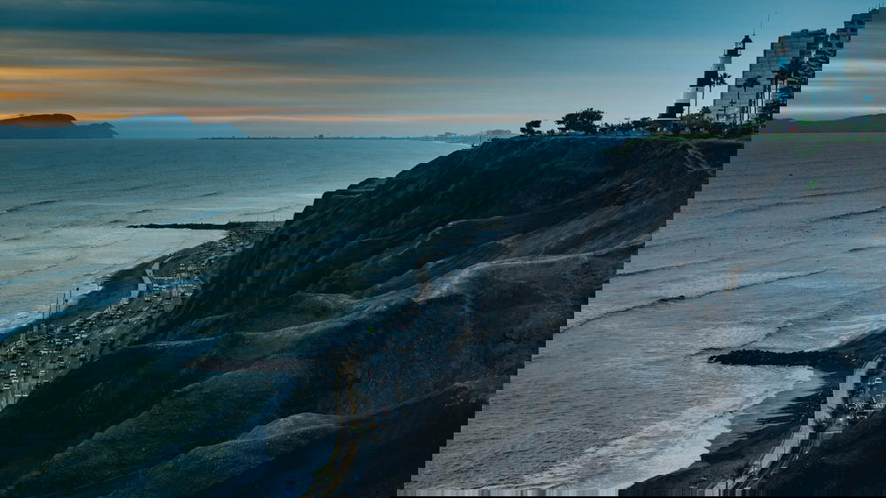 Gloomy sunset at black seaside cliffs with a black and white lighthouse and buildings
