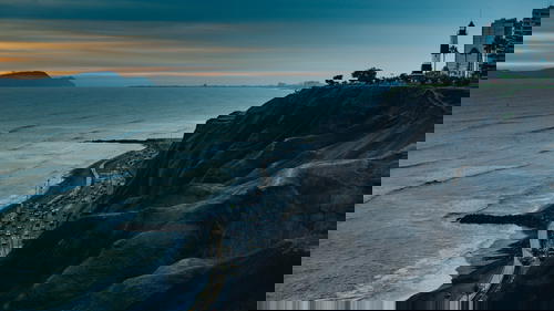 Gloomy sunset at black seaside cliffs with a black and white lighthouse and buildings