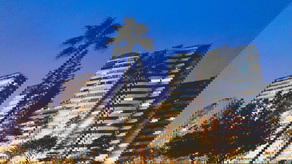 A city at night in Peru with tall buildings and palm trees.