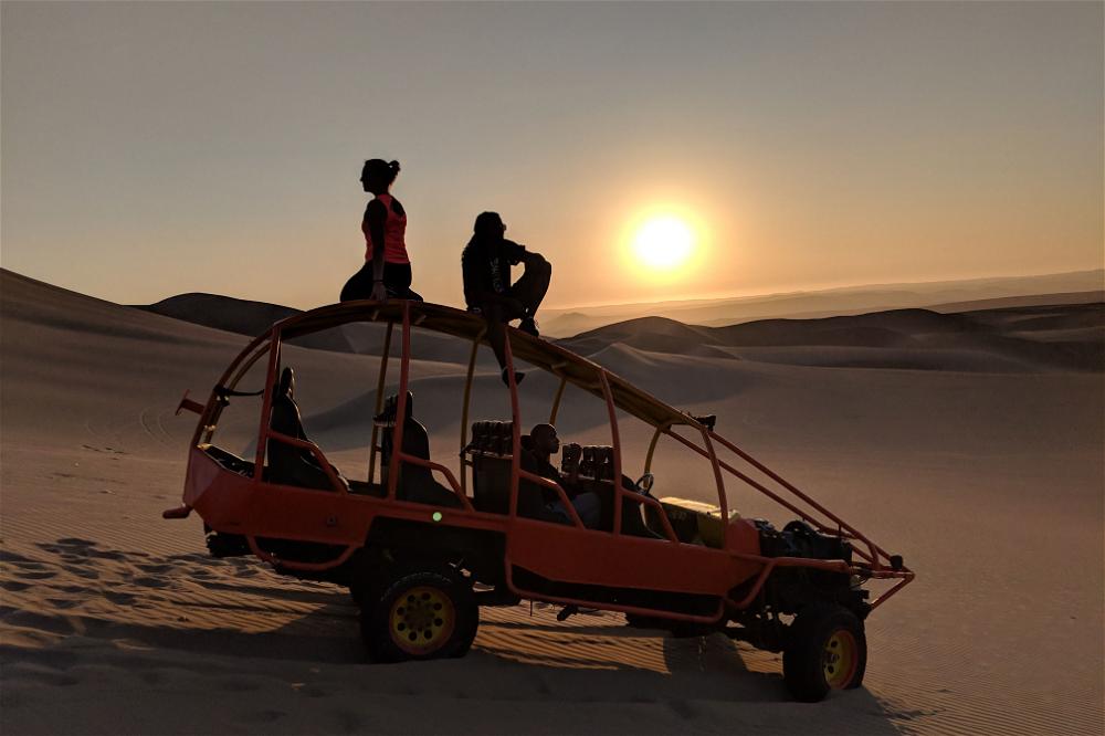 A group of people are sitting on top of a jeep in the desert.