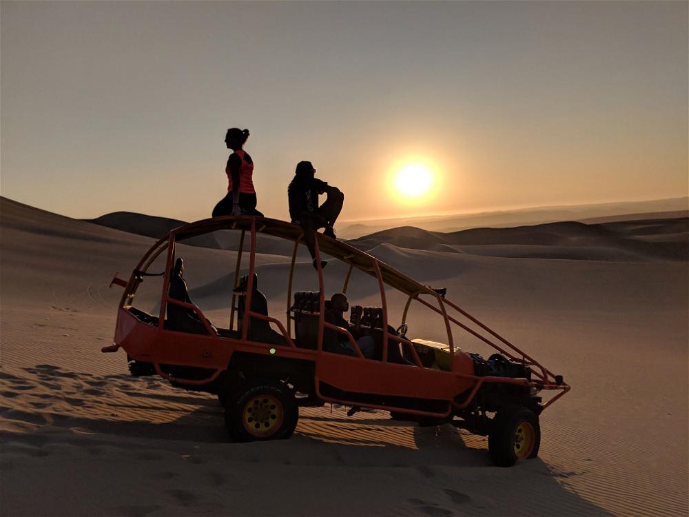 A group of people are sitting on top of a jeep in the desert.