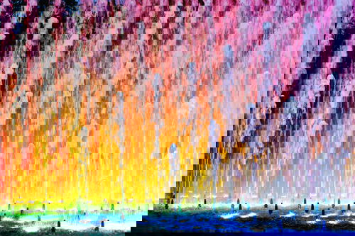 Water fountain shooting vertical streams of water against neon lights