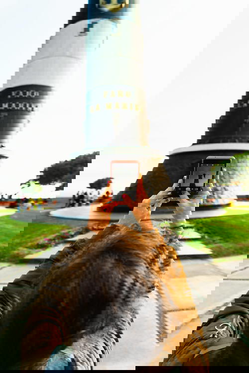 Woman holding up a cell phone to take a photo of a black and white lighthouse