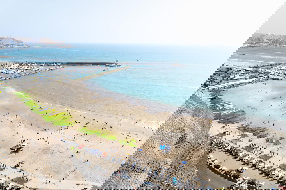 Seaside cliffs next to a white beach and a blue sea and hazy sky