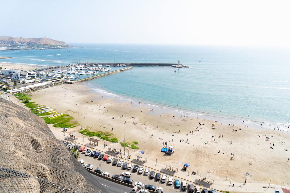 Seaside cliffs next to a white beach and a blue sea and hazy sky