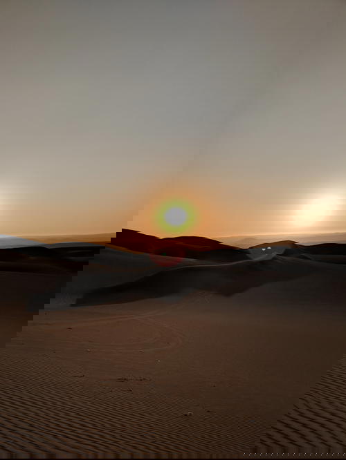 Sunset with the sun close to the horizon against sand dunes