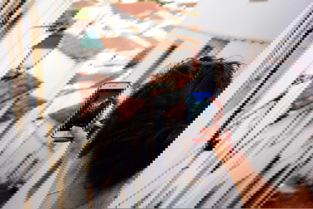 Women holding up a cell phone to take a photo of depth in a Portuguese village of white houses