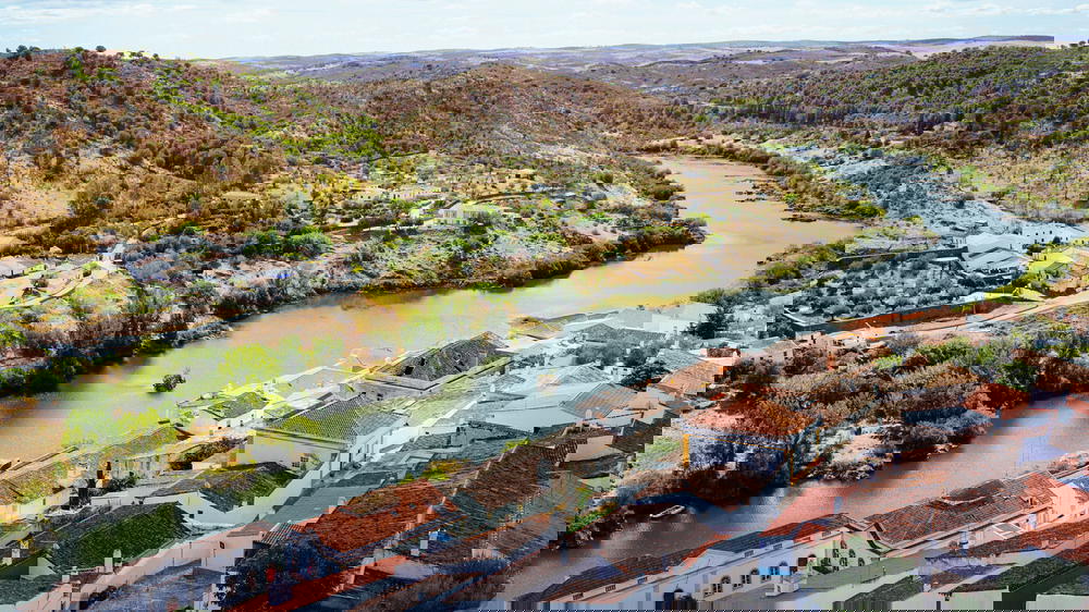 Red tiled roofs of white houses along a winding river dotted with green trees