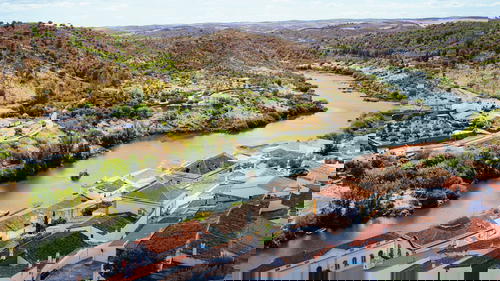 Red tiled roofs of white houses along a winding river dotted with green trees