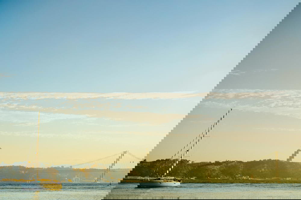 A sailboat in the water with a bridge in Portugal.