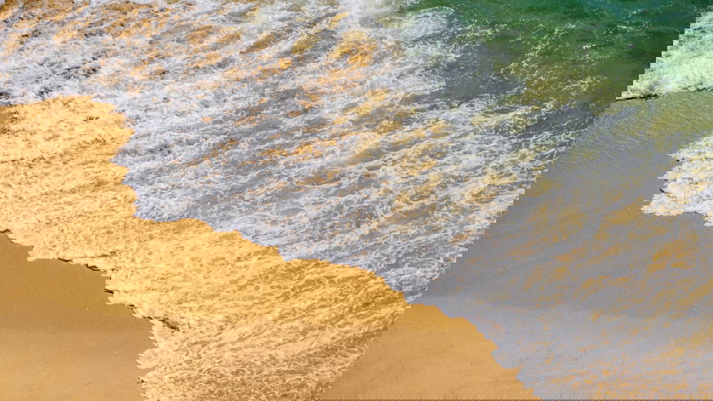 An aerial view of an ocean wave on a sandy beach in Portugal.
