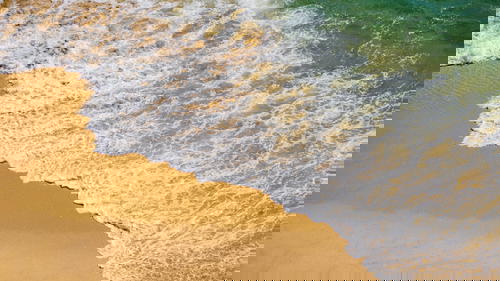 An aerial view of an ocean wave on a sandy beach in Portugal.