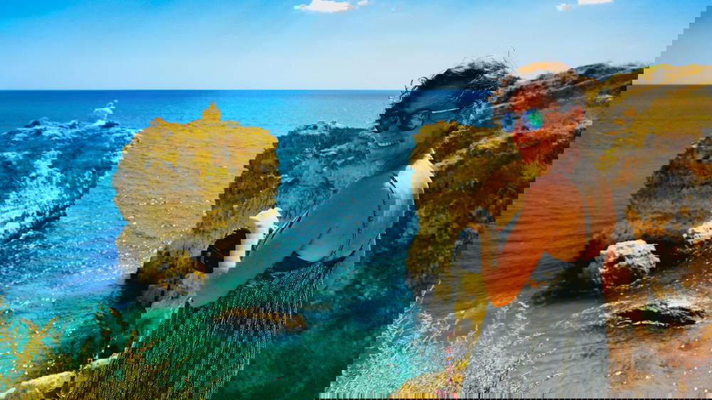 A woman with turquoise and blue waters at a sandy beach with rock formations in Portugal