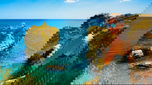 A woman with turquoise and blue waters at a sandy beach with rock formations in Portugal