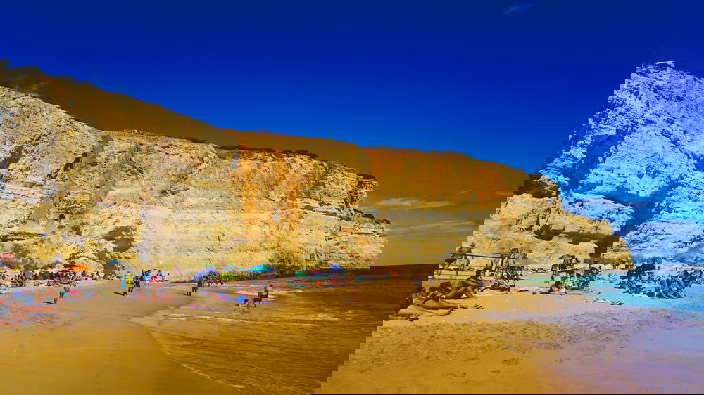 A crowded beach with cliffs in the background in Portugal.