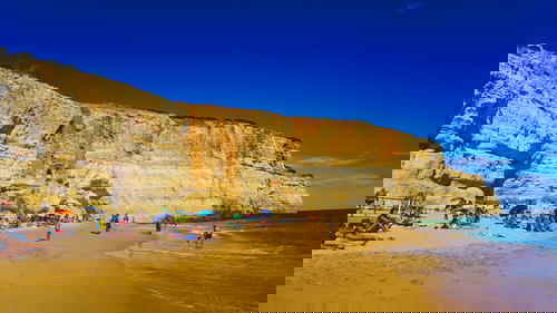 A crowded beach with cliffs in the background in Portugal.