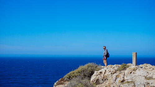 A person standing on a cliff in Portugal overlooking the ocean.