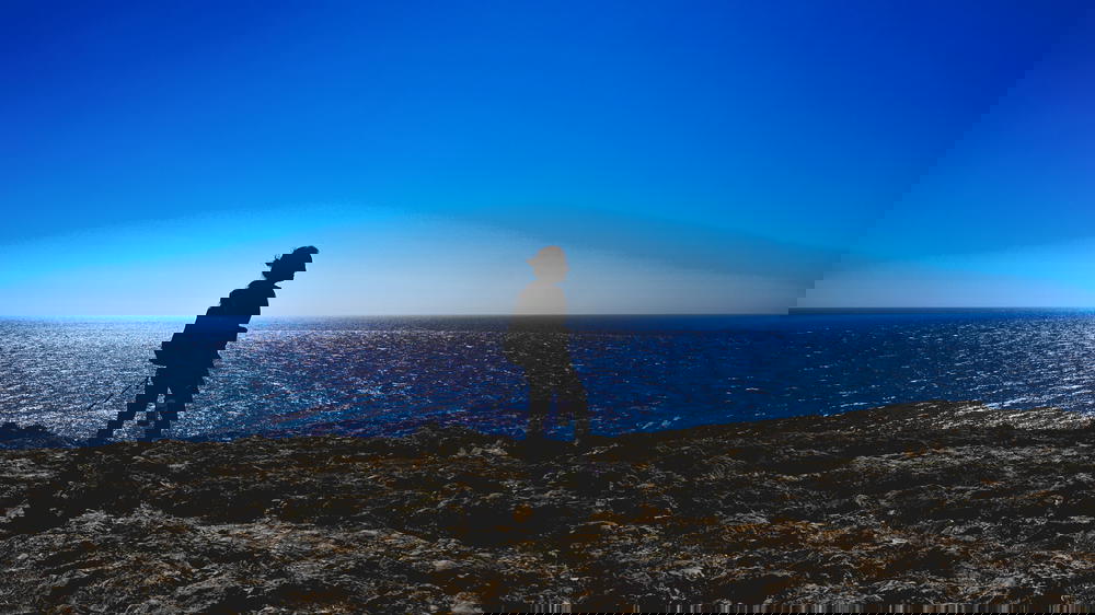 A silhouette of a man standing on top of a cliff overlooking the ocean in Portugal.