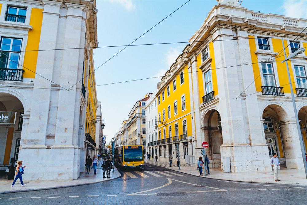 A yellow bus driving down a Lisbon city street in Portugal.