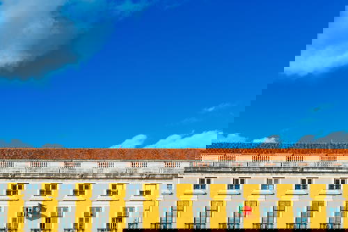 Yellow facade of a historic Portuguese building and red tiled rooftop against bright blue sky