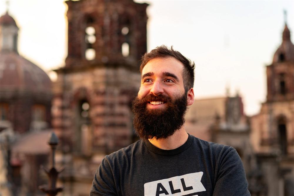 A man with a beard smiling in front of a building.