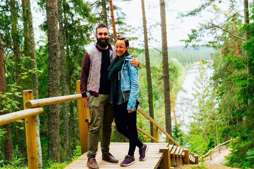 A man and woman standing on a wooden walkway in the forest.