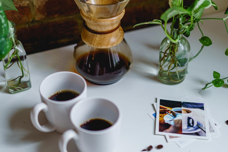 Two cups of coffee on a table next to a plant.