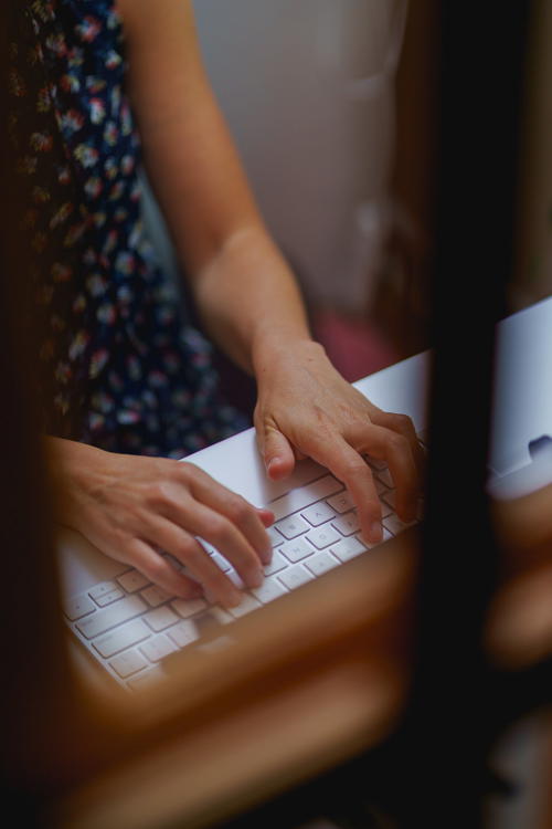 Woman typing on an Apple Magic keyboard at a white desk table in a home office
