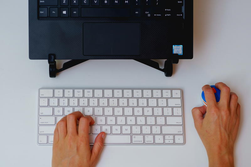 A woman's hands typing on a keyboard next to a mouse.